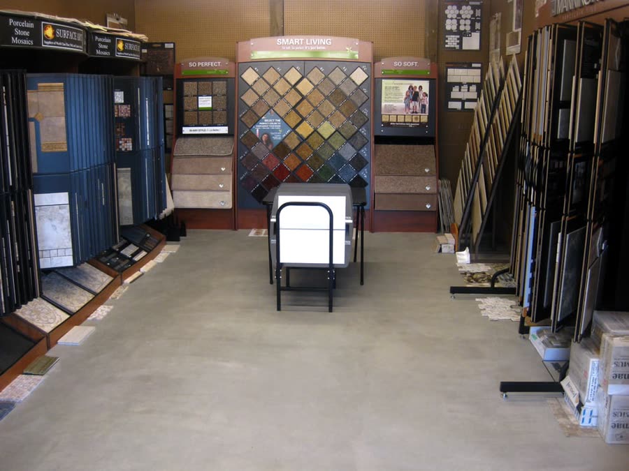 Inside the Mobile Floor Coverings showroom on Hammer Drive in Bellingham,
                  with sample display racks down both sides and a tile mosaic wall at the end.