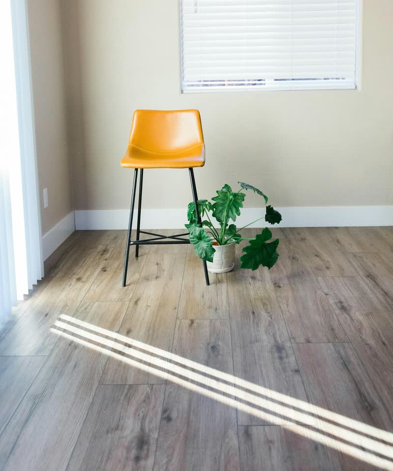A bright room with a grey-brown plank floor, a yellow stool and a potted plant.