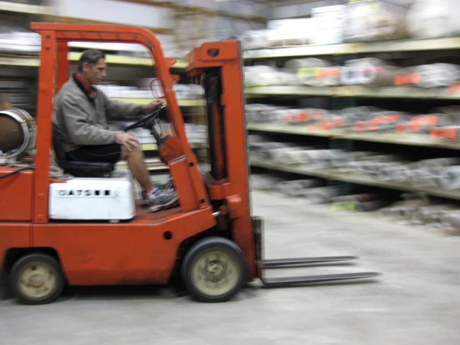 A forklift moving down an aisle of racked carpet rolls in the Mobile Floor
                  Coverings warehouse in Bellingham.
