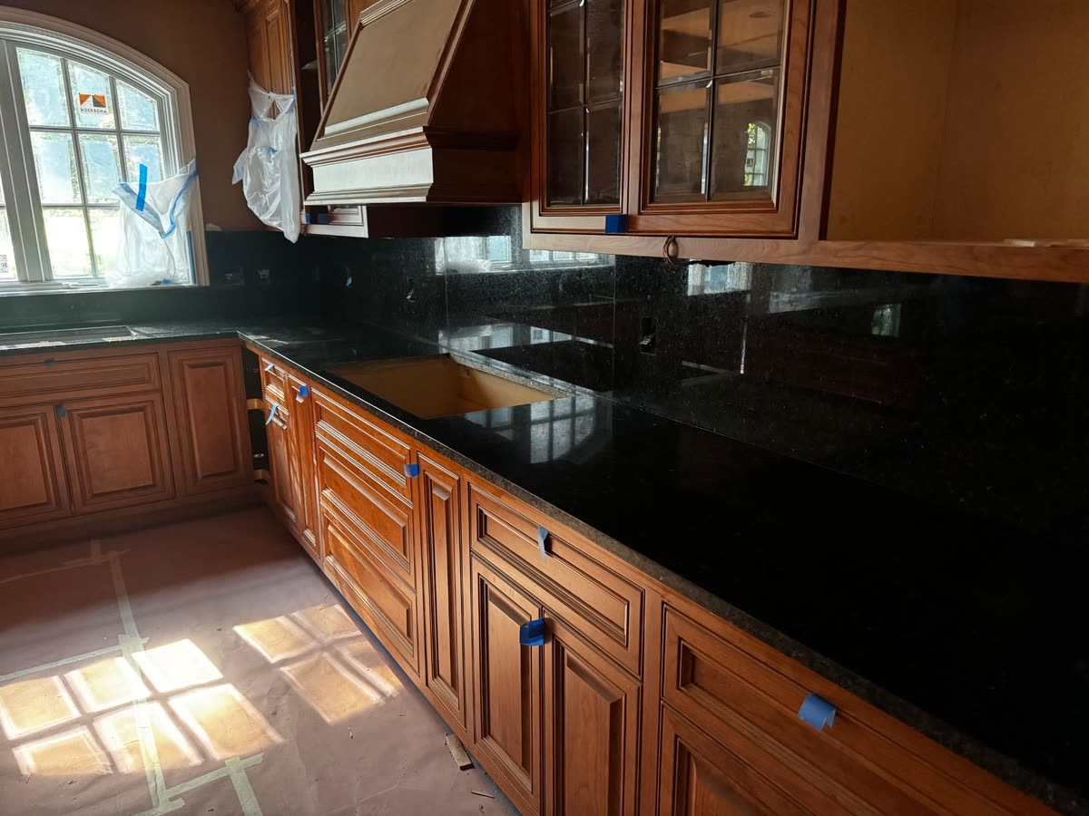 Dark stone counters and a full-height splash in a kitchen with cherry-coloured cabinets, blue tape still on the doors.