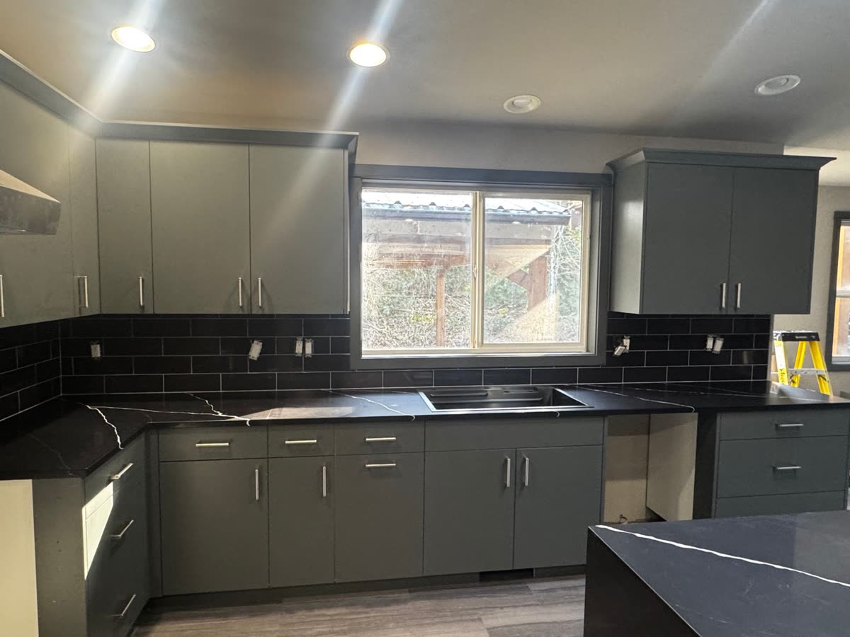 A kitchen with dark green cabinets, black subway tile and black counters, sink cut out.