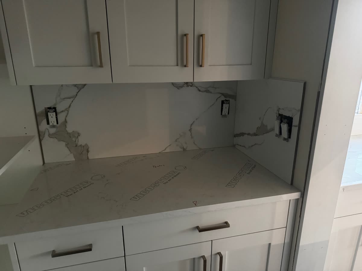 A pantry counter and matching splash in pale veined quartz, protective film still on the top.